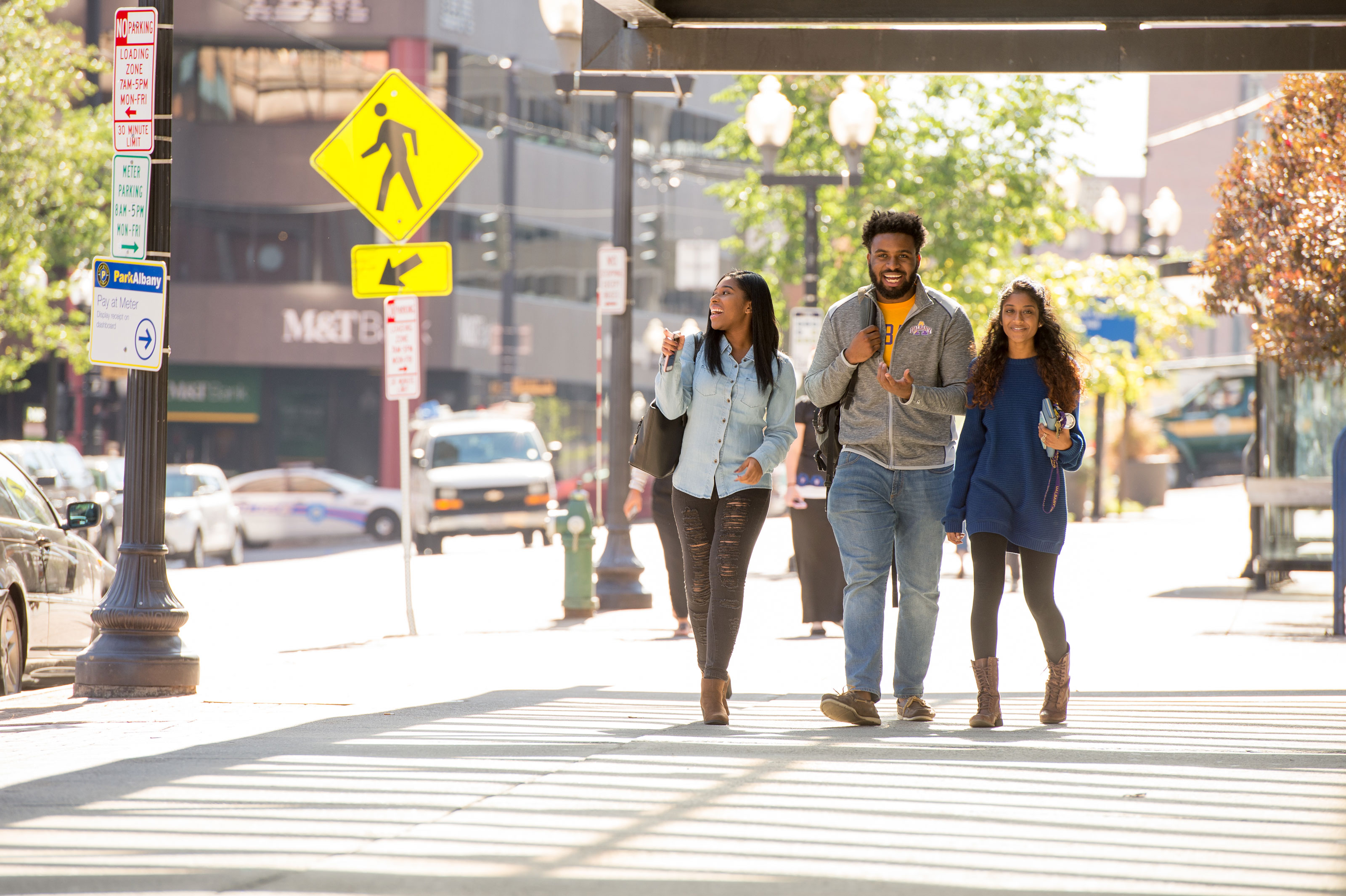 Three students smile and laugh as they walk down a Downtown Albany sidewalk.